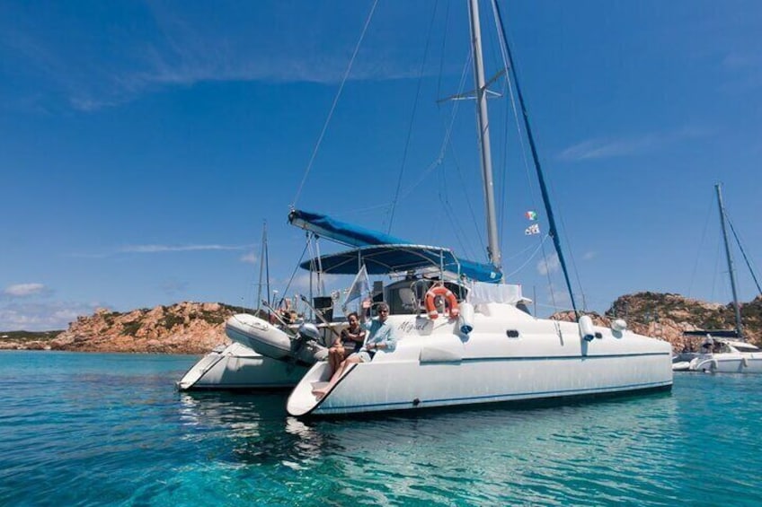 A white catamaran with a blue canopy and passengers enjoying the water. 2