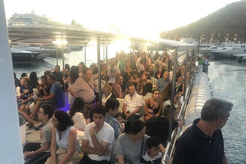 Un bote lleno de gente sentada, una masa de agua y un barco grande al fondo. 4