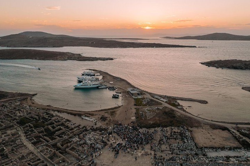 A coastal area with a large crowd, boats, and a historical site. 2