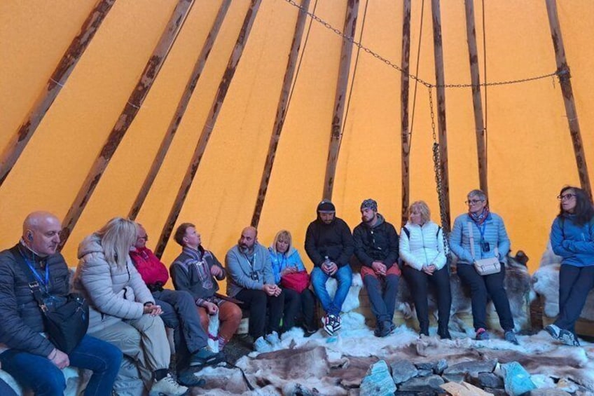 A group of people sitting inside a wooden tent with a snowy ground. 5