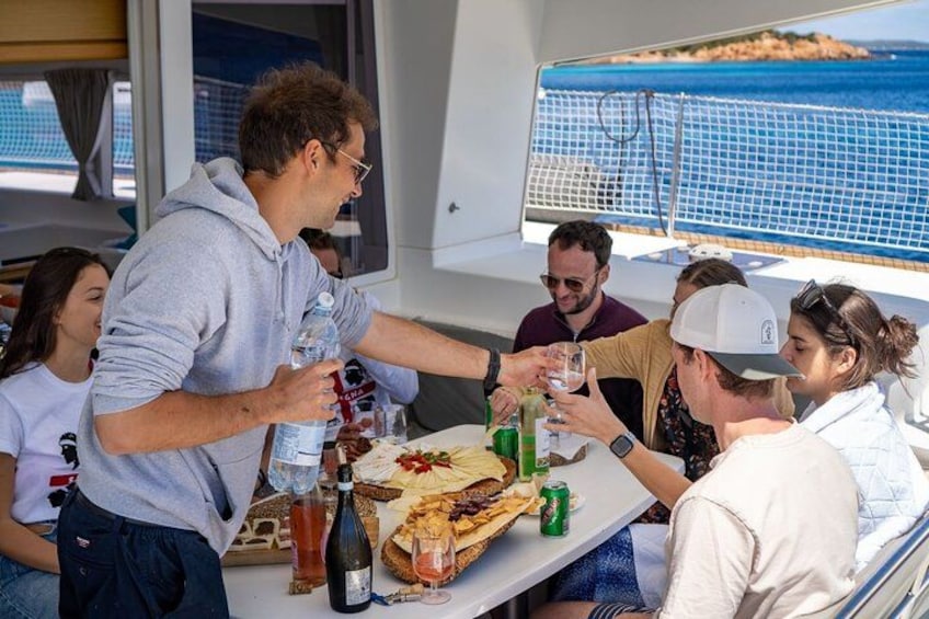 En gruppe mennesker skåler med drikkevarer på en båd med udsigt til havet. 5