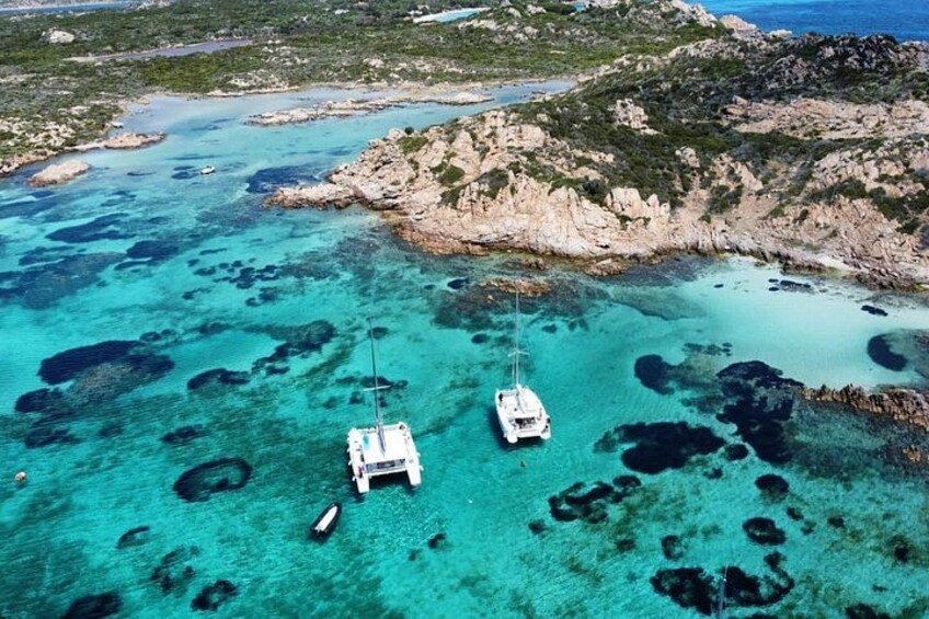 Een kustgebied met helder turquoise water, rotsachtig terrein en twee boten afgemeerd nabij de kust. 4