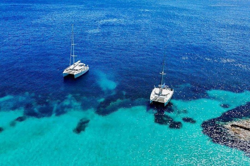 Twee zeilboten geankerd in helder turquoise water, met zichtbare koraalriffen. 2