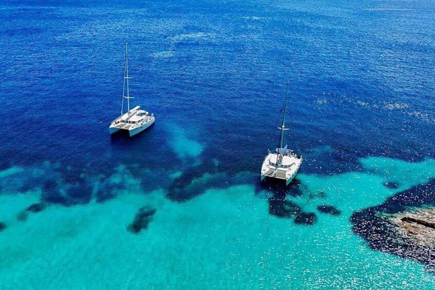 Two sailboats anchored in clear turquoise waters with visible underwater formations. 4