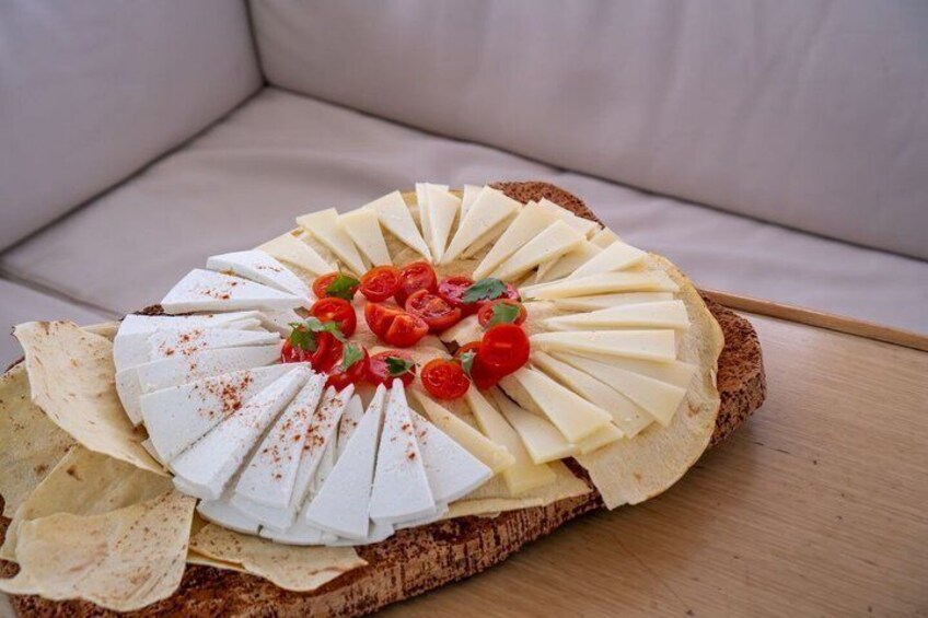 Una tabla de quesos sobre madera, con una rebanada de pan, tomates cherry y un toque de especias rojas. 3
