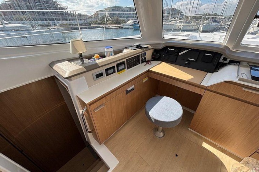 A boat's interior with a control panel, a small seating area, and a view of the marina outside. 5