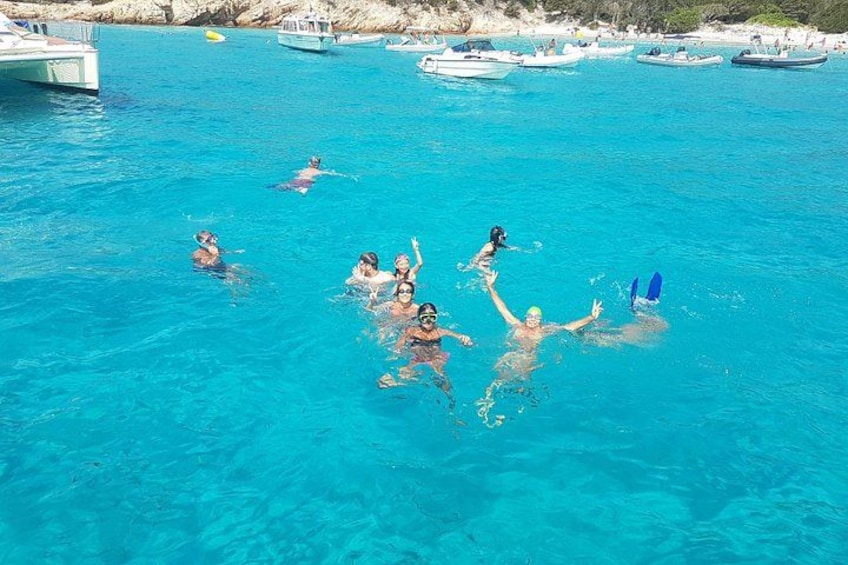 Personas nadando en un mar azul y transparente, con barcos al fondo. 4