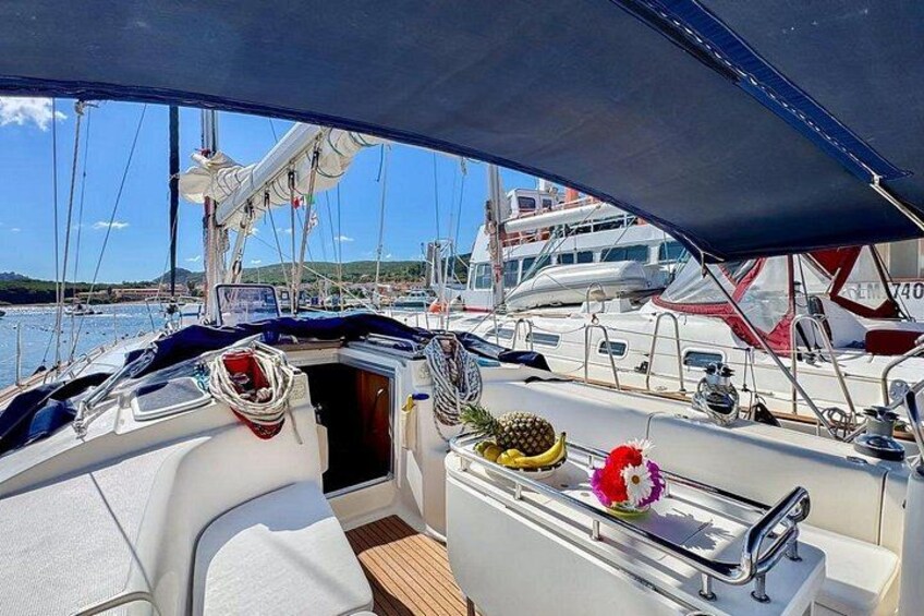 A boat deck with white seating, a small table with a fruit bowl, and a flower arrangement. 3
