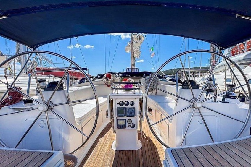 A sailboat's deck with a steering wheel, control panel, and wooden flooring. 4