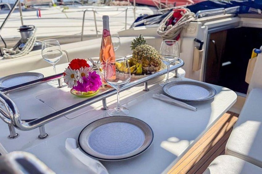 A dining table on a boat with plates, glasses, a bottle, and a pineapple. 2