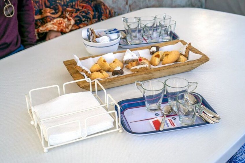 A table with a tray of pastries, a bowl of utensils, and a tray of shot glasses. 4