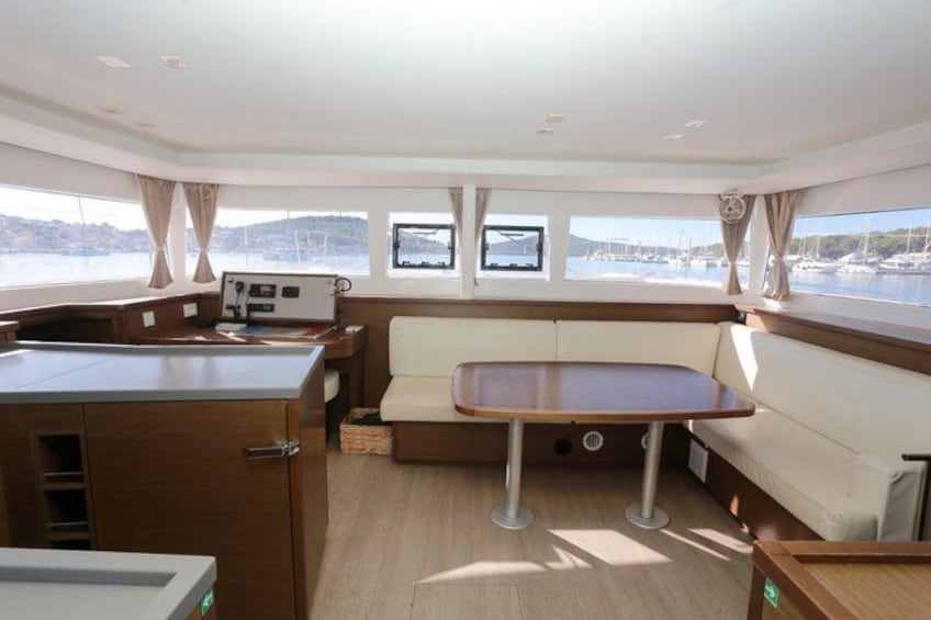 A boat interior with a dining area, windows, and a control panel. 5
