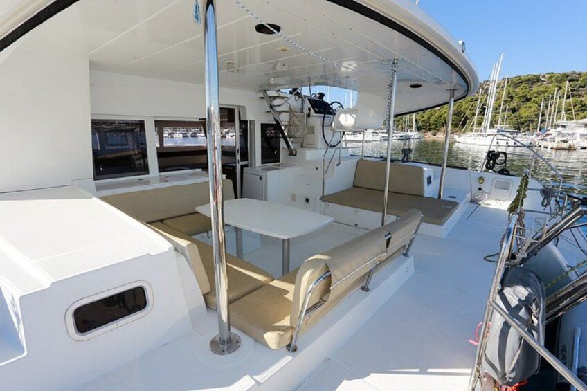 Ein Bootsdeck mit Sitzgelegenheiten, einem Steuer und einem Yachthafen im Hintergrund. 2