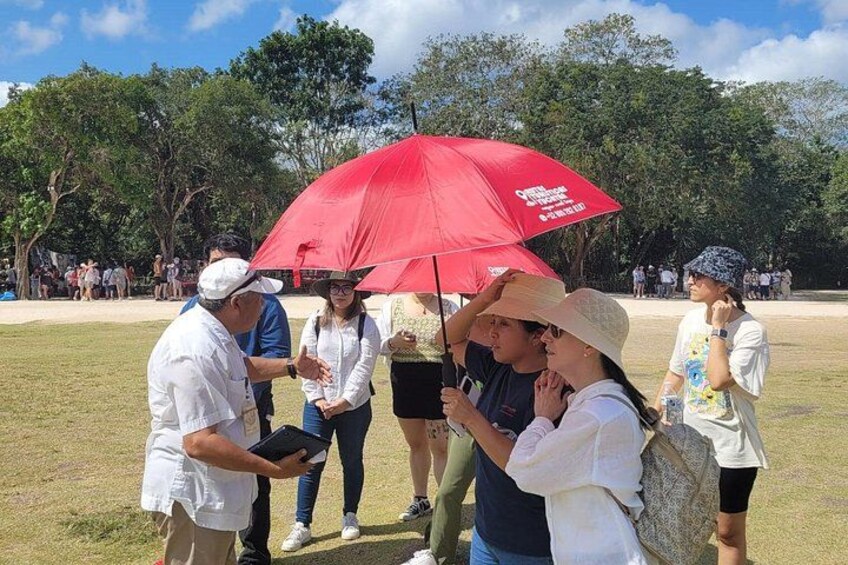 Un grupo de personas de pie en un parque con un paraguas rojo, árboles y un campo cubierto de césped. 3