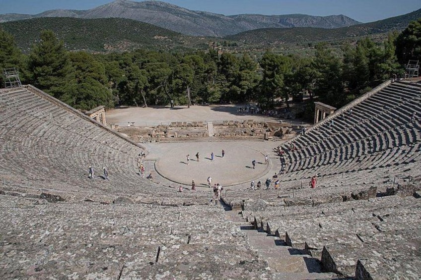 An ancient amphitheater with stone seating and ruins in the center. 1