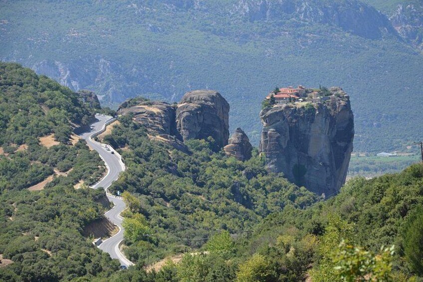 A winding road through a mountainous landscape with rocky cliffs and dense greenery. 3
