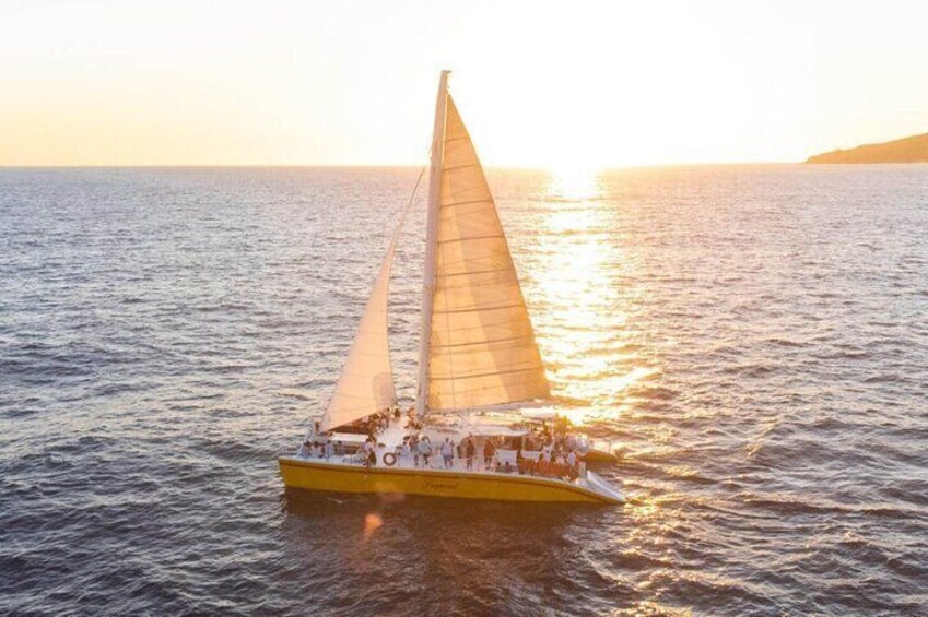 A yellow sailboat with passengers on a calm sea at sunset. 1