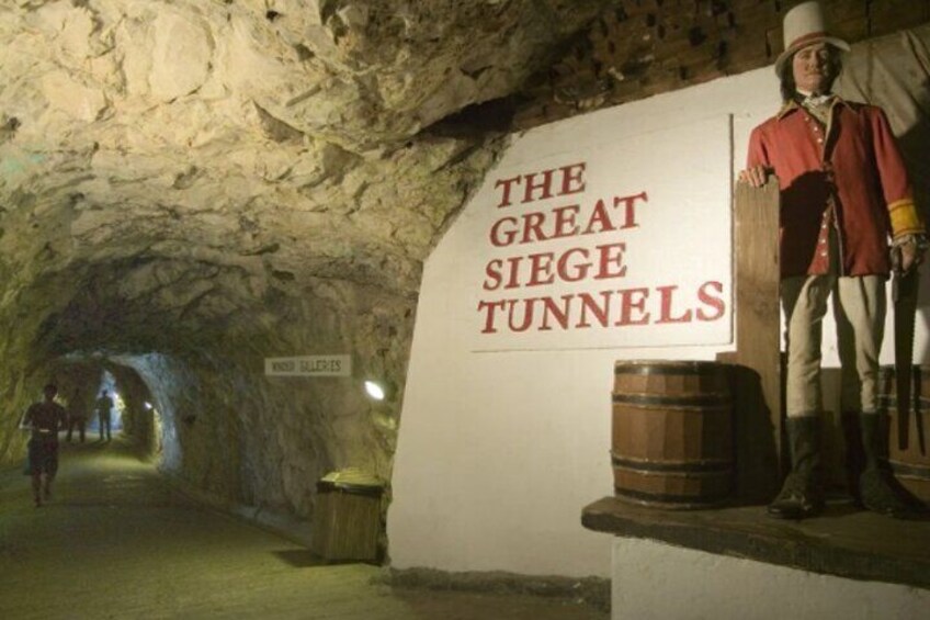 Eine historische Ausstellung mit einer Wachsfigur in historischer Kleidung, einem Schild mit der Aufschrift 'THE GREAT SIEGE TUNNELS' und einem Fass. 2