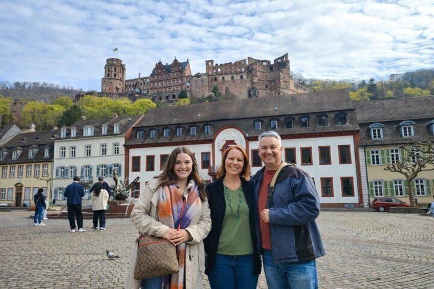 A cobblestone square with historic buildings, a castle in the background, and a few people. 5