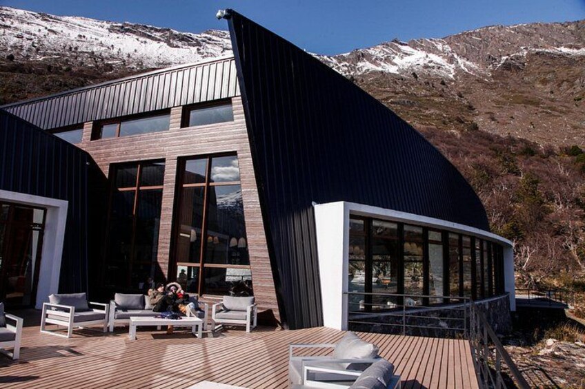 A modern building with a curved roof, large windows, and a wooden deck with outdoor furniture. 4