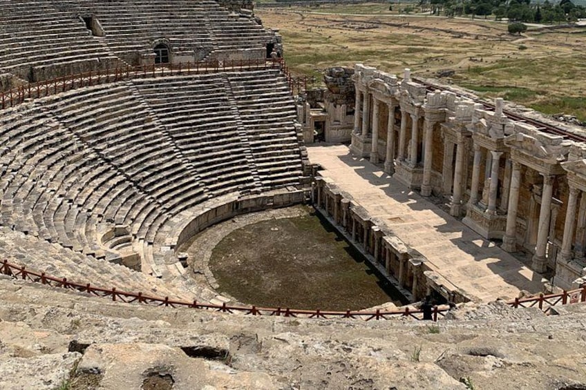 Un antiguo anfiteatro con asientos en niveles escalonados y un escenario central. 3