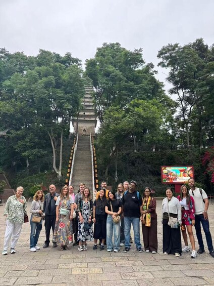 A group of people standing in front of a large stone staircase leading up to a pagoda, surrounded by lush green trees. 5