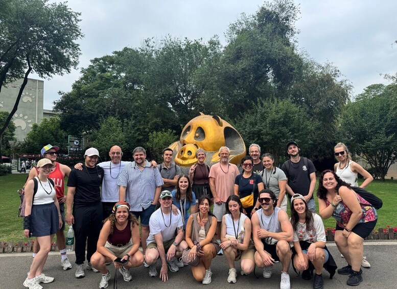 A group of people posing in front of a large, yellow, cartoonish statue of a pig in a park. 3