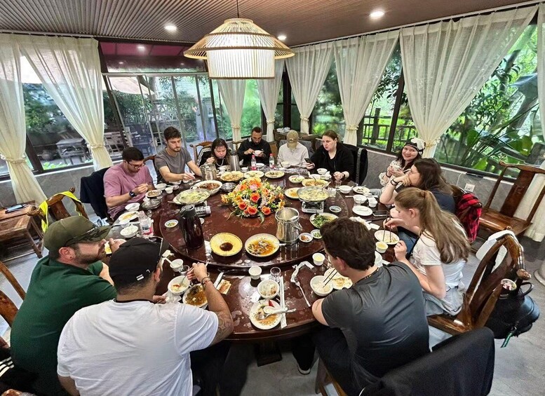 A group of people dining around a large round table with various dishes and a decorative centerpiece. 4