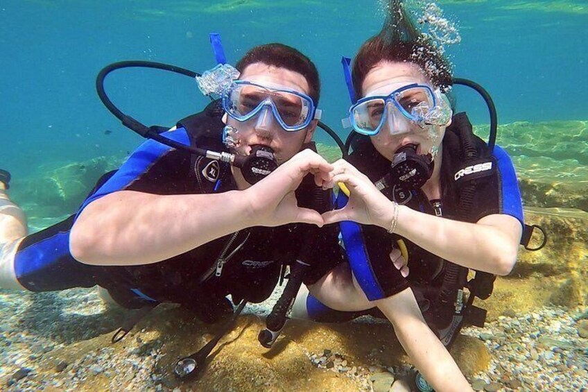 Two scuba divers underwater making a heart shape with their hands. 1