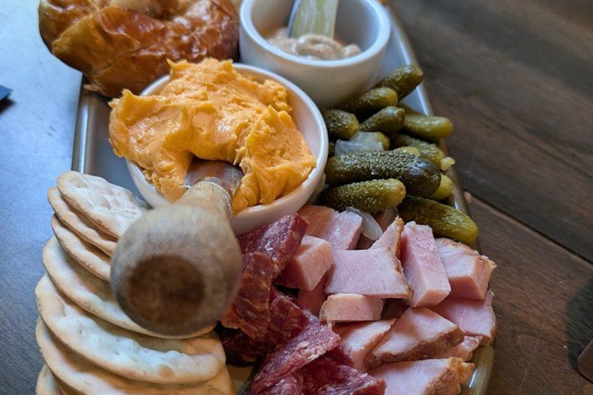 A charcuterie board with various meats, pickles, and a bowl of mustard. 2