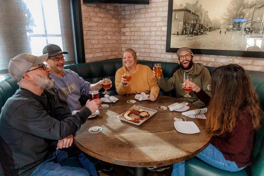A group of people sitting around a round table in a brick-walled room, holding drinks and eating. 3