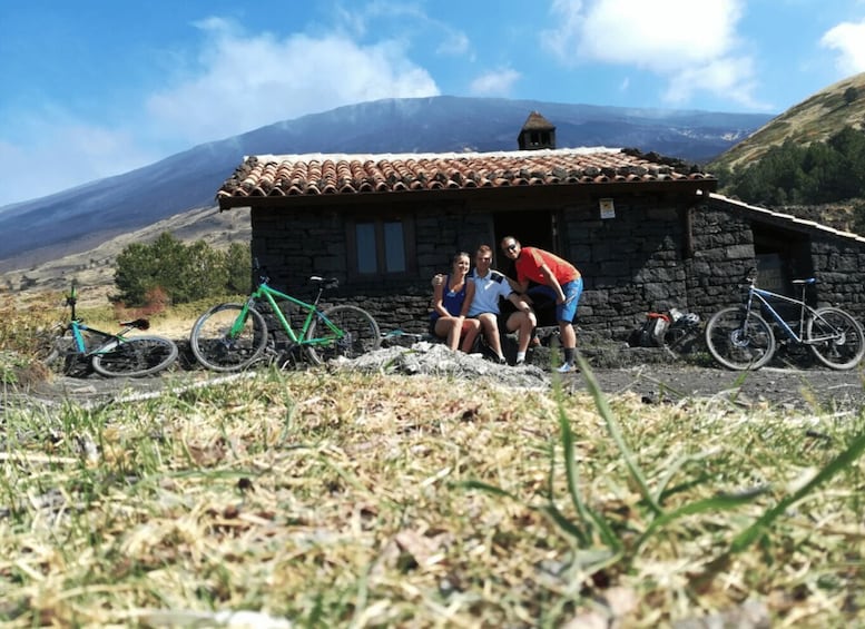A stone building with a tiled roof, surrounded by bicycles and people in a mountainous landscape. 2