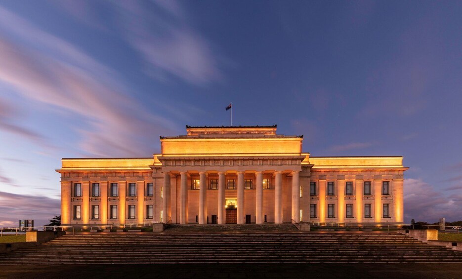 A large, classical building with a flag on top, illuminated by warm lights, and surrounded by a set of stairs. 2