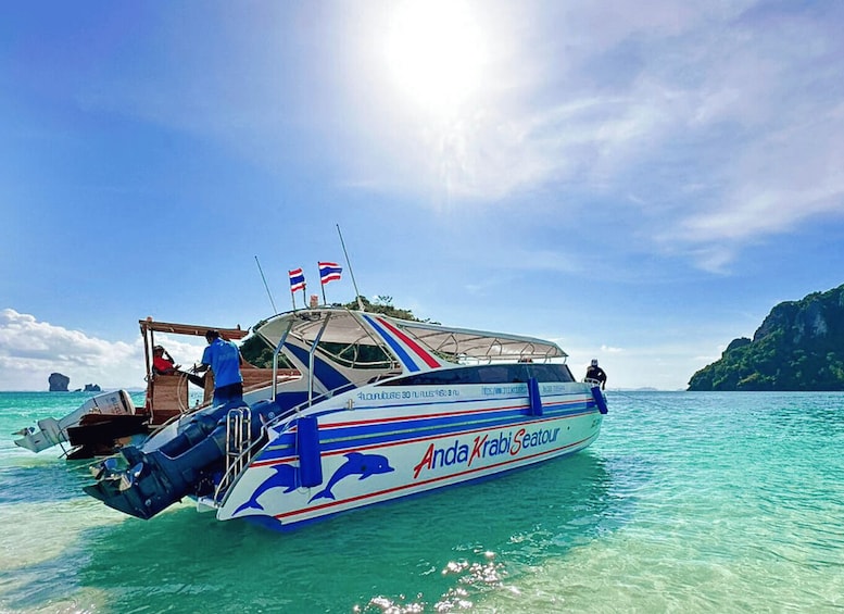Veneen nimi on ’Anda Krabi Seatour’, ja siinä on kaksi lippua, katettu kansi sekä henkilö, joka seisoo keulassa. 4