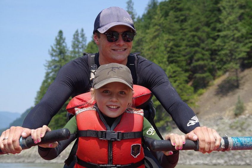 A person carrying a child on their back, both wearing life jackets, holding onto a handlebar. 4
