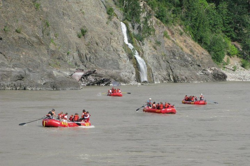 A group of people rafting on a river with a waterfall in the background. 3