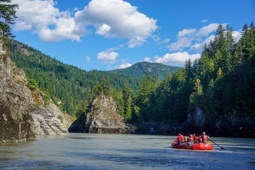 A group of people rafting on a river surrounded by forested mountains. 1