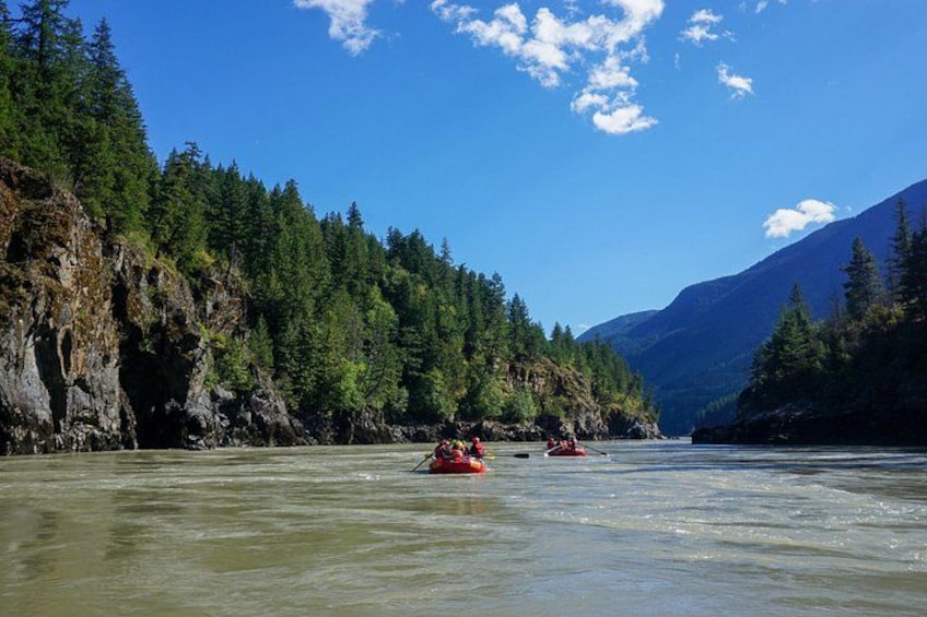 A river with kayaks, surrounded by dense forest and mountains. 2