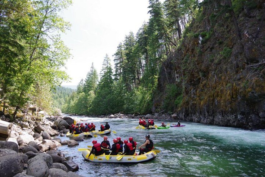 Un groupe de personnes fait du rafting sur une rivière, entouré de falaises abruptes couvertes de forêts. 2