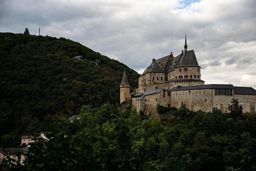 A historic castle on a hill with a prominent tower, surrounded by dense greenery. 2