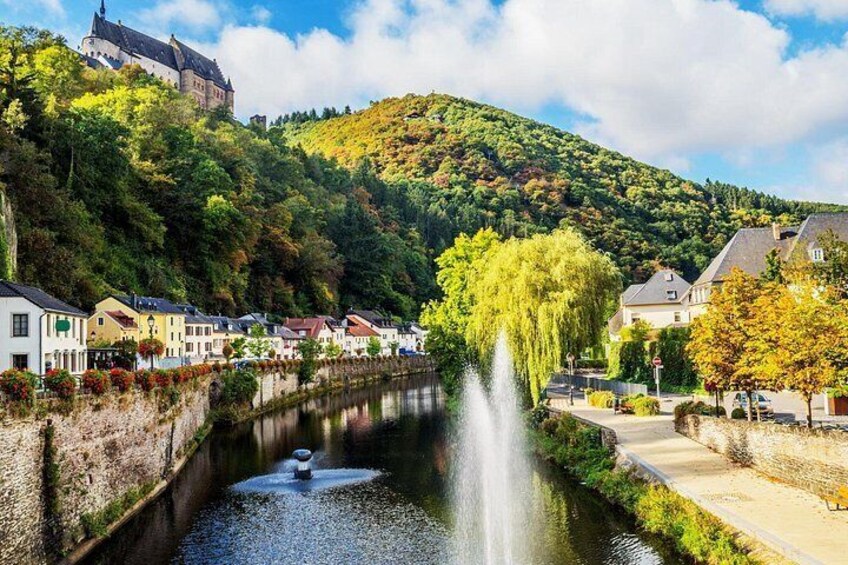 A river with a fountain, houses along the riverbank, and a castle on a hill. 3