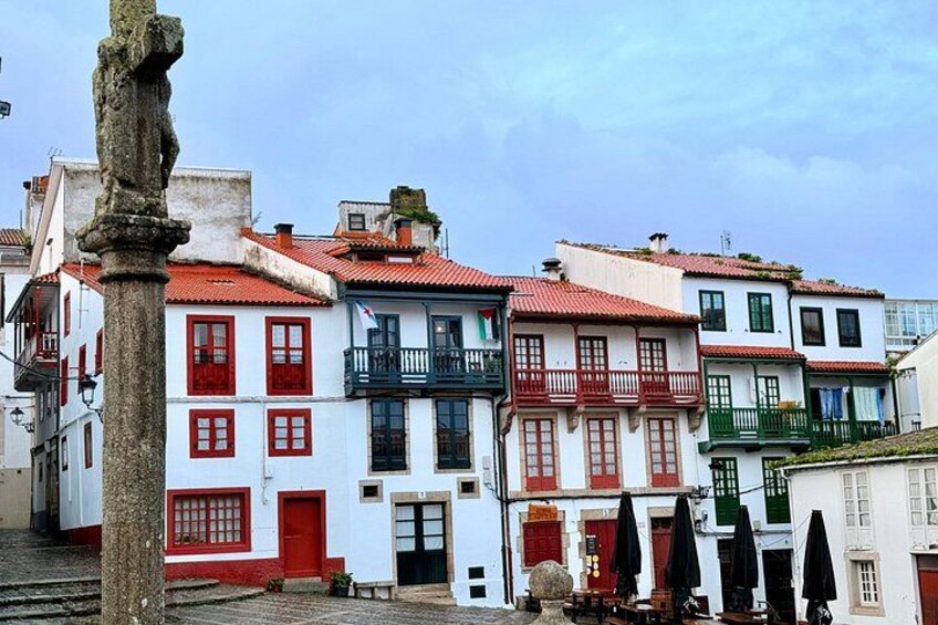 A row of colorful buildings with red and white facades, a stone column, and a street with umbrellas. 2