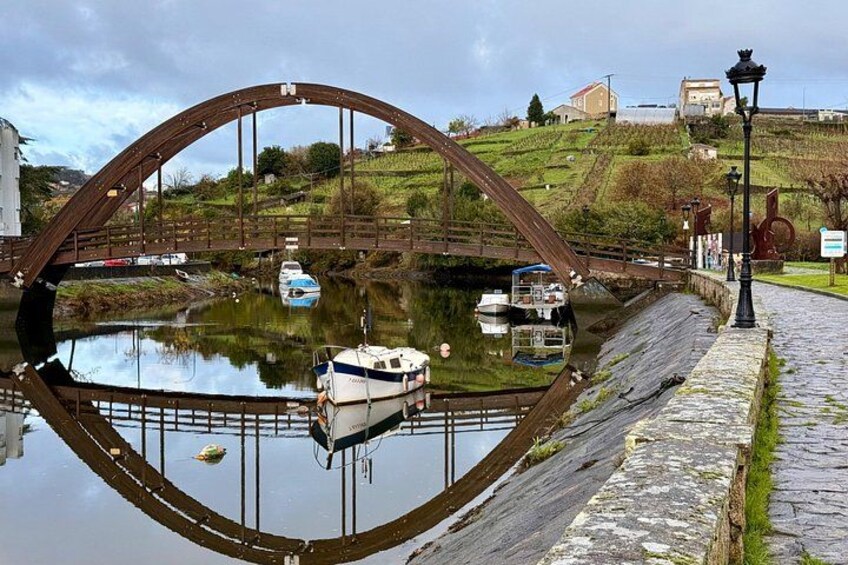 A river with boats, a wooden bridge, stone pathway, and a hill with buildings in the background. 3