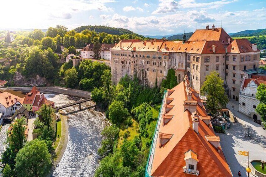 A historic castle with a river in the foreground, surrounded by lush greenery and a clear sky. 1