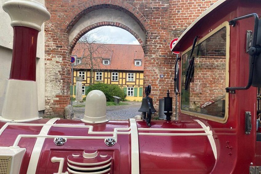 A red train engine with white trim, a brick archway, and a yellow building with a red roof in the background. 4