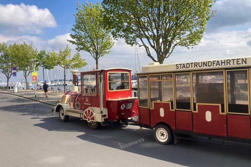 A vintage tram with 'STADTTRUNDFAHREN' on its side, parked on a street with trees and a clear sky. 3