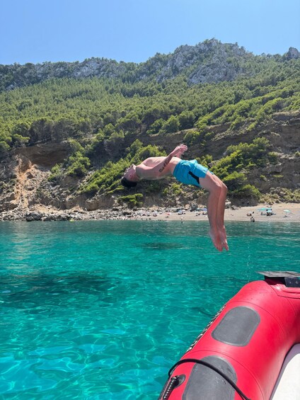 A person diving into turquoise water from a rocky cliff with a forested hillside in the background. 4
