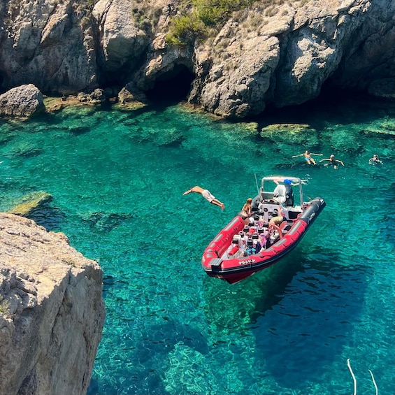 A red inflatable boat on clear turquoise water surrounded by rocky cliffs. 1