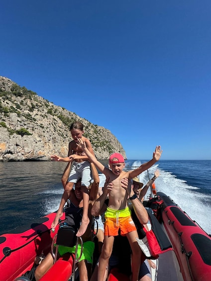 A group of people on a red boat with rocky cliffs and clear blue water in the background. 5