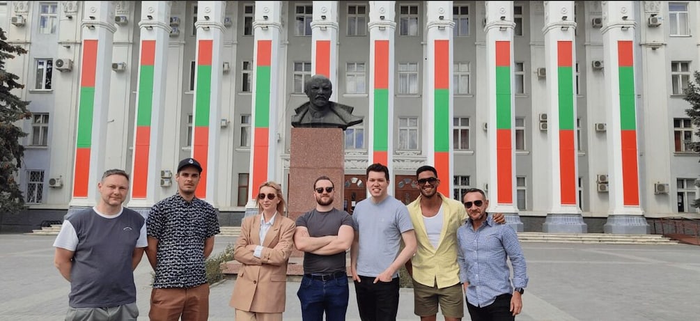A group of people standing in front of a building with columns and a statue. 4